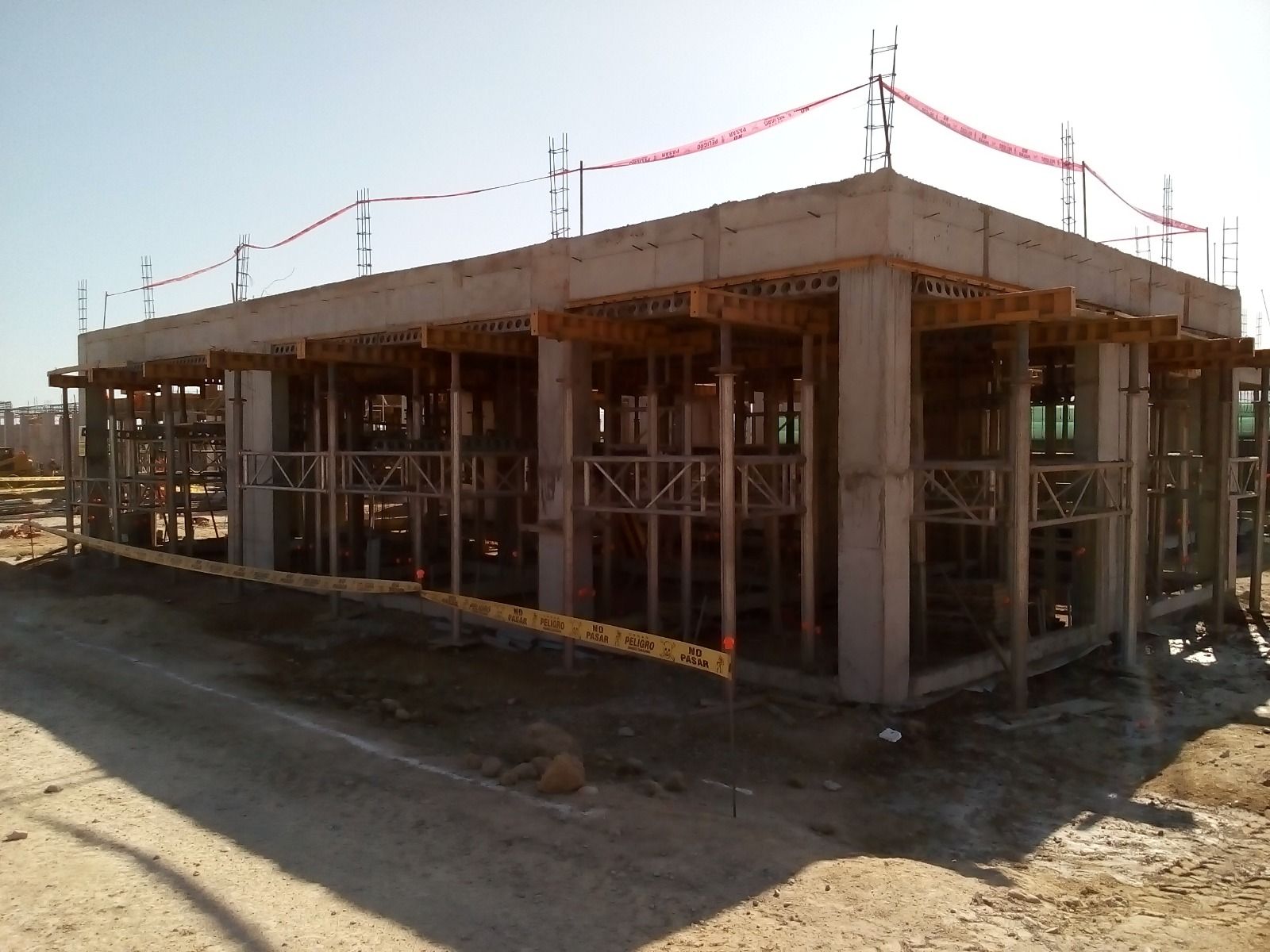 Edificio de hormigón parcialmente construido con andamios y barandillas de seguridad en la azotea en una obra de construcción.