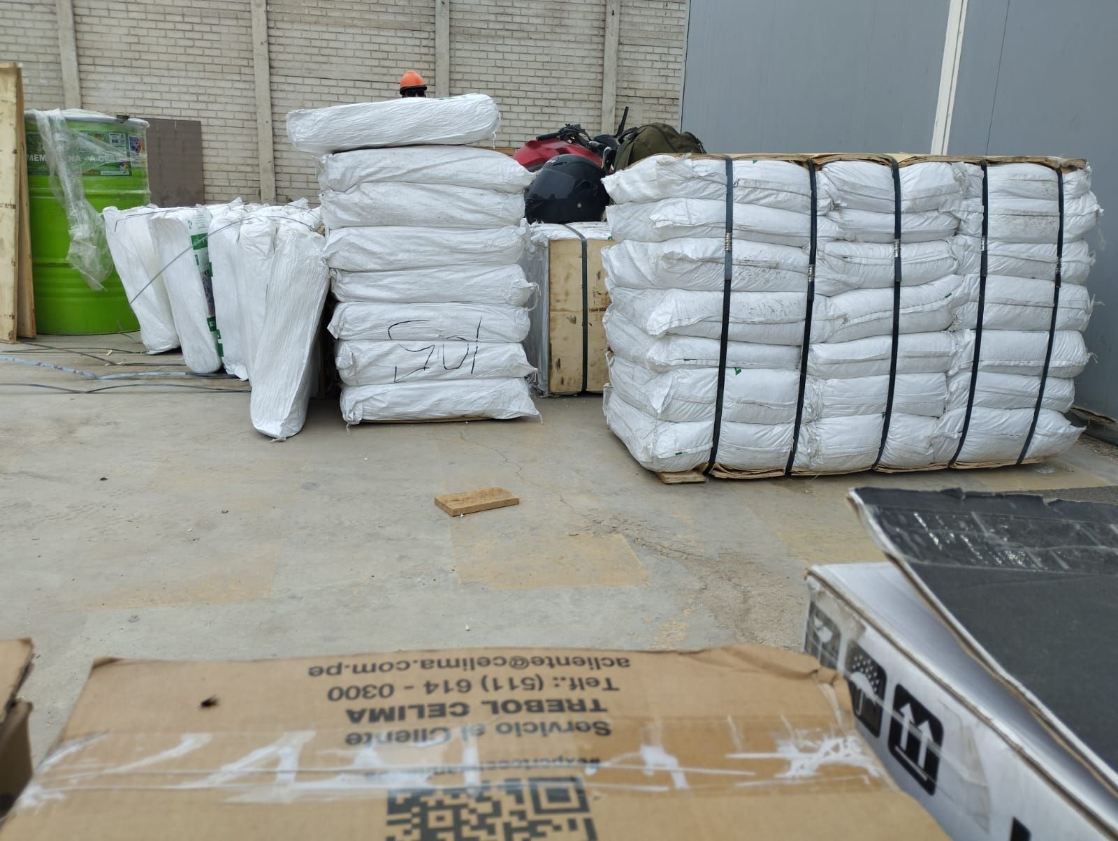 Pacas blancas envueltas apiladas en una zona de almacén, con palés y cajas en el suelo.