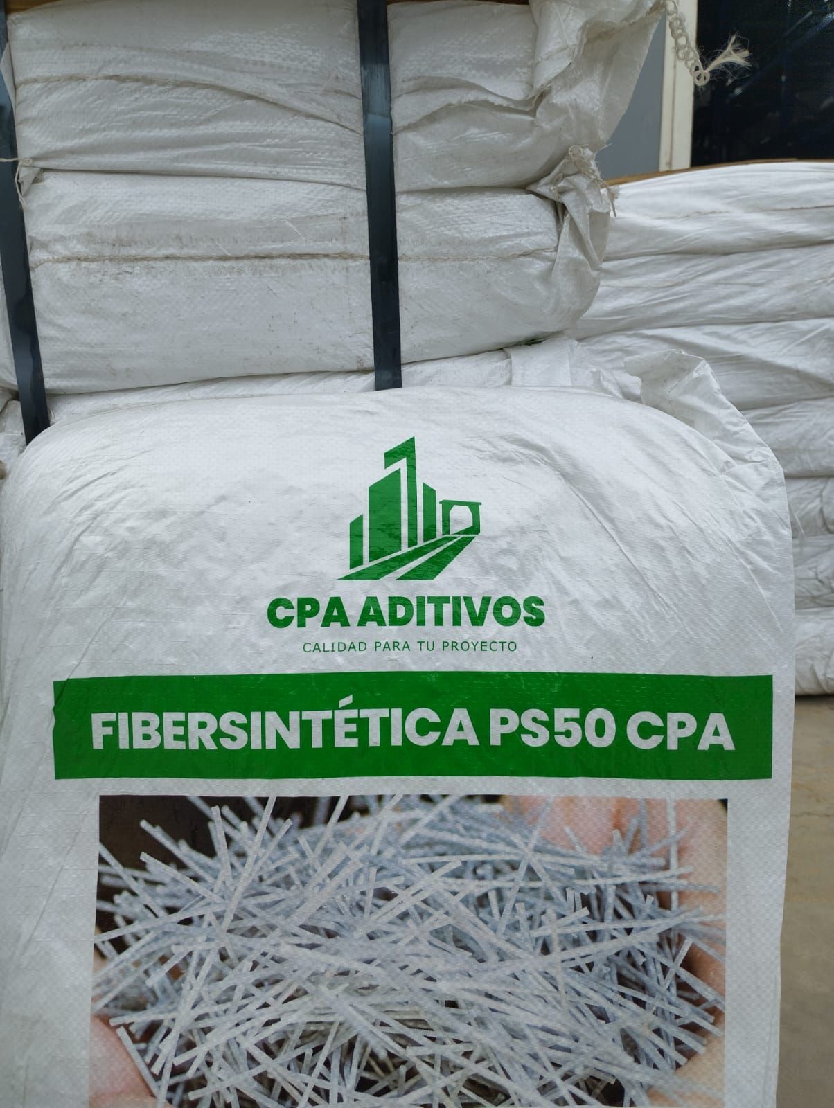Bolsa blanca con la etiqueta “CPA ADITIVOS FIBERSINTÉTICA PS50 CPA” y sacos apilados al fondo.