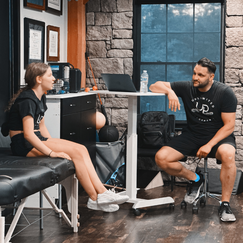 Two people talking in a gym in Gibbsboro, NJ a black chair, table, and stone wall.