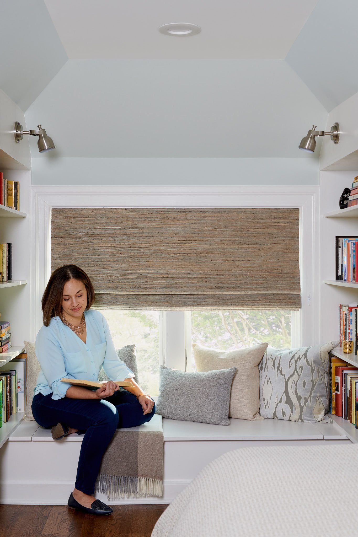 A woman is sitting on a window seat reading a book.