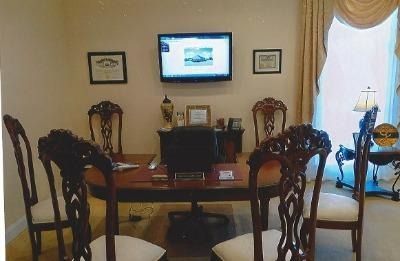 Dining room with wooden table, ornate chairs, wall-mounted TV, and a bright window with drapes.