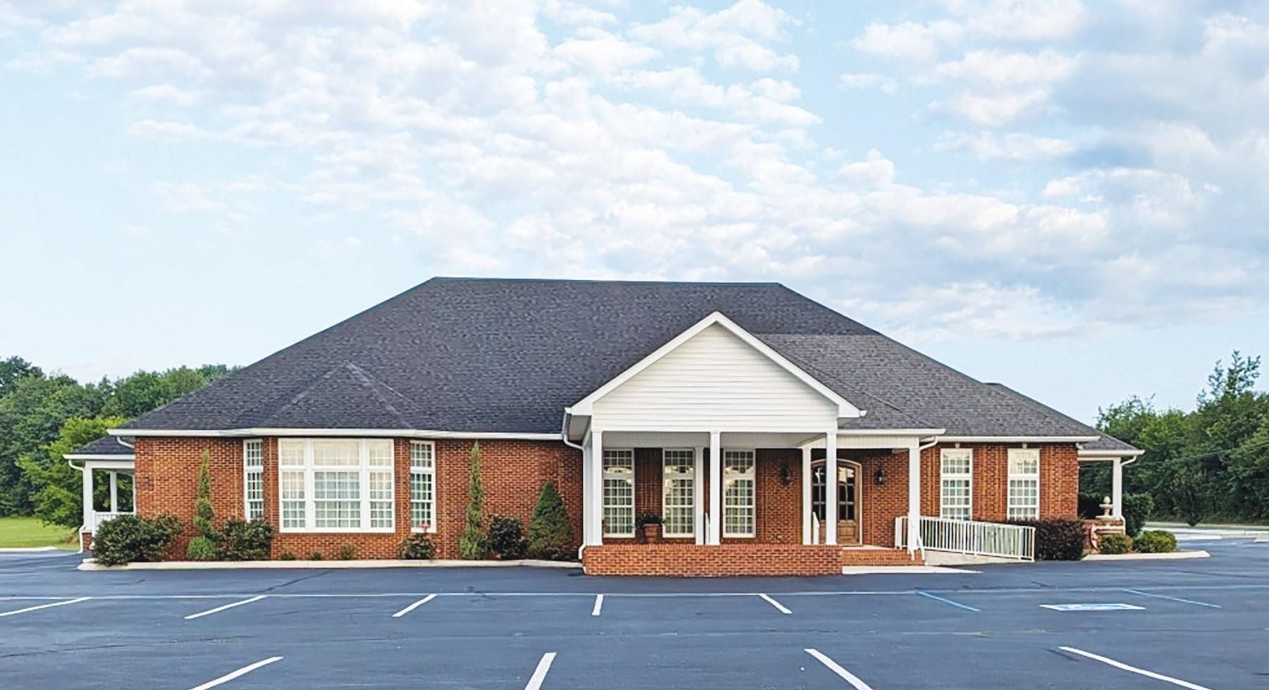Brick office building with white columns and a dark roof, seen from an empty parking lot.