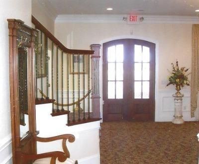 Interior entryway with curved staircase, double wooden doors, and a decorative vase on a carpeted floor.