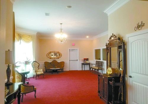 Spacious lounge with red carpet, cream walls, chandeliers, sofas, and a large mirror near a white door.