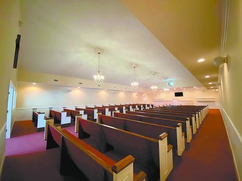 Empty church pews in a warmly lit sanctuary with purple carpet and white walls