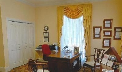 Home office with desk, red chair, white door, and yellow curtains over a bright window.