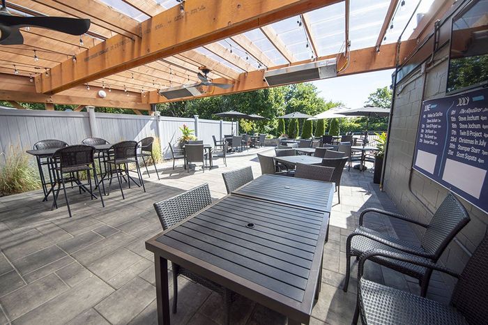 Outdoor patio dining area with metal tables and chairs under a wooden pergola on a sunny day.