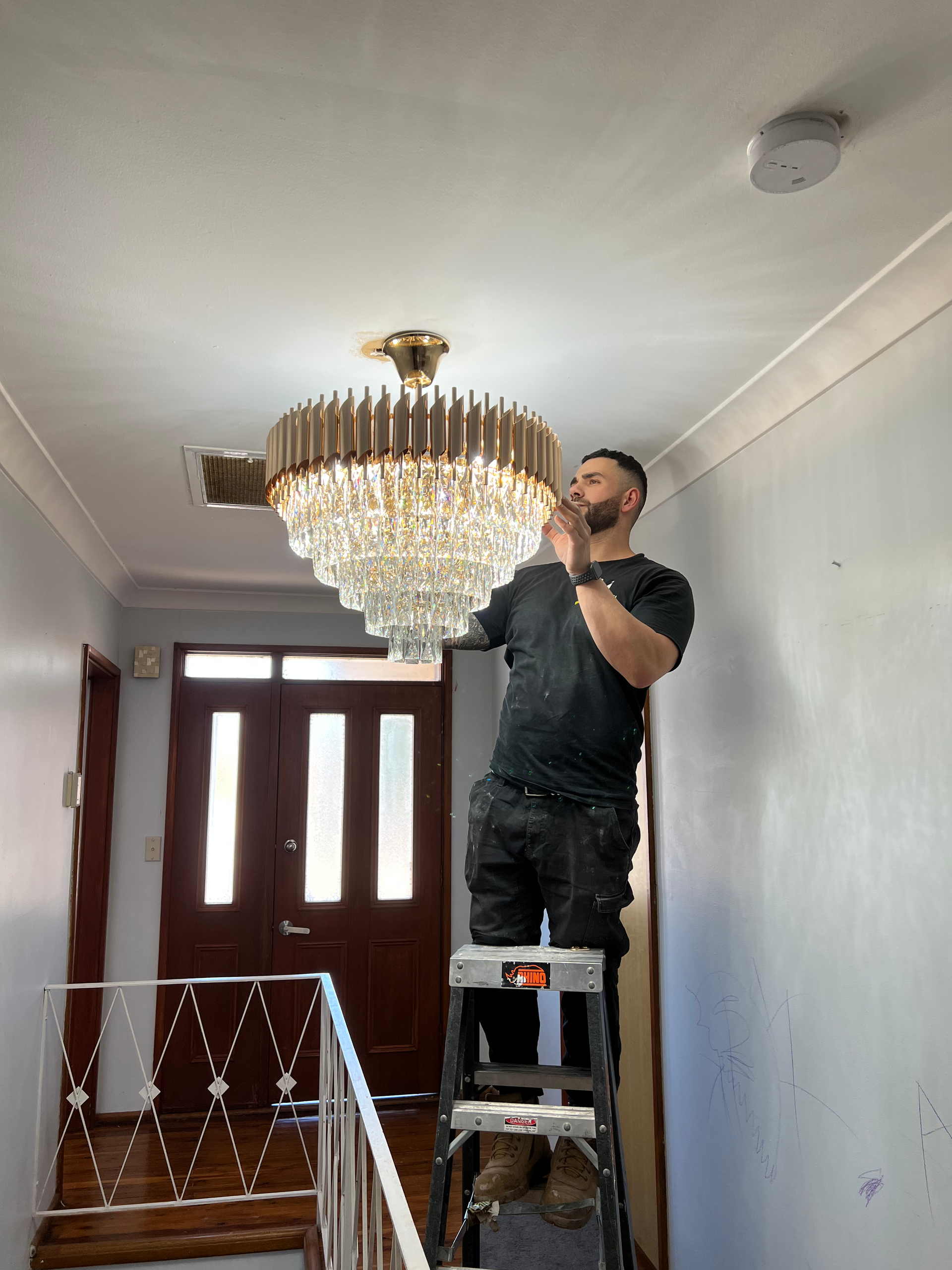 A man is standing on a ladder fixing a chandelier.