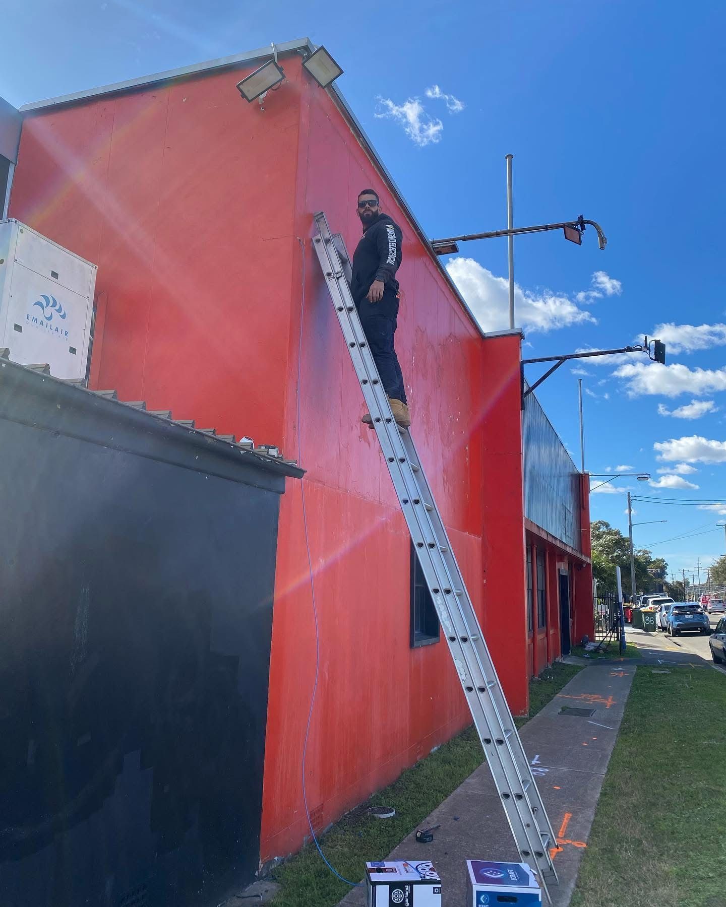 A man is standing on a ladder painting a red building.