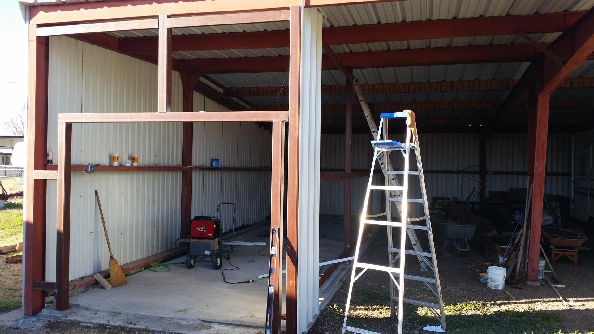 Open metal shed with tools and a ladder under a red roof, in a partially finished garage.