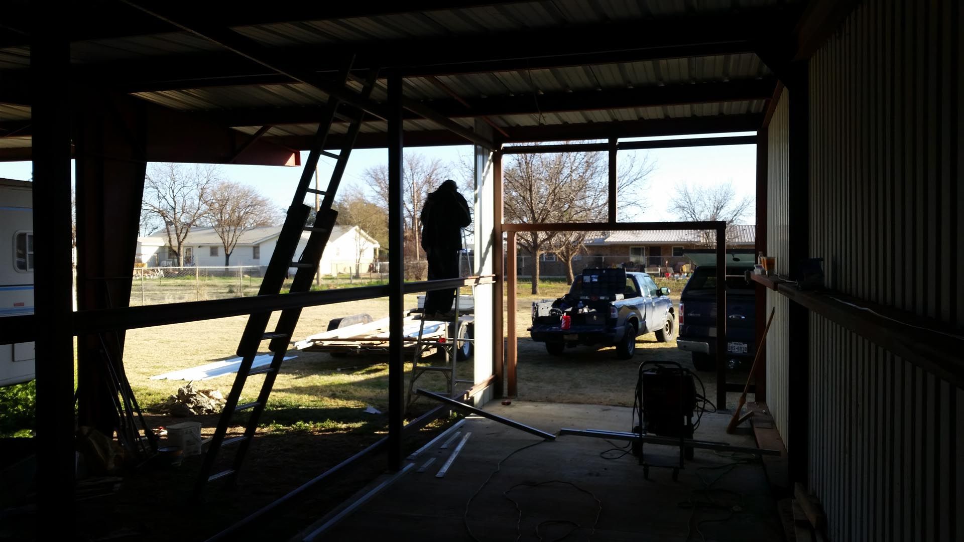 Silhouetted worker inside a barn-like structure, with a ladder and construction equipment near an open doorway