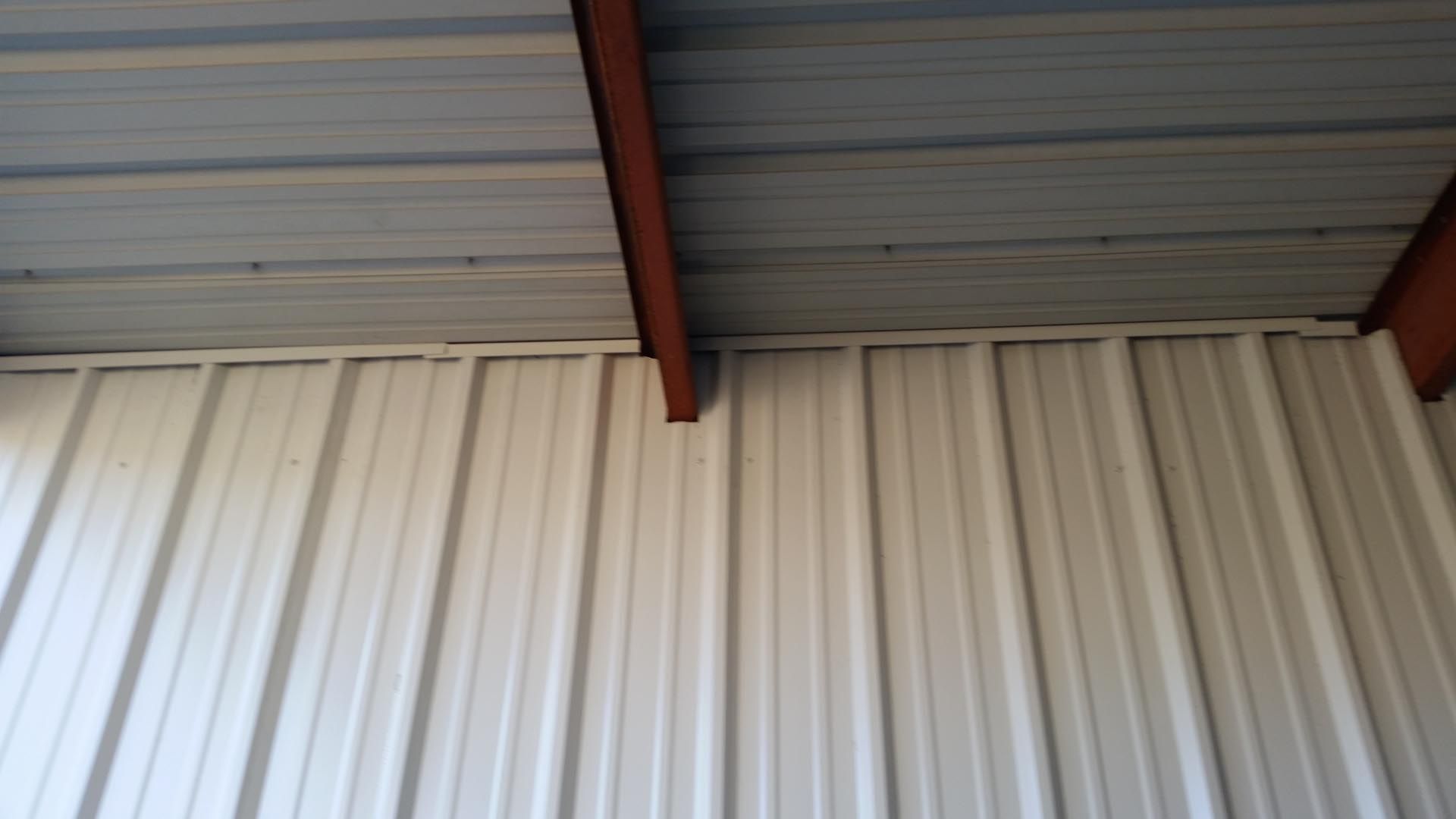 White corrugated wall beneath a gray metal roof with red beams