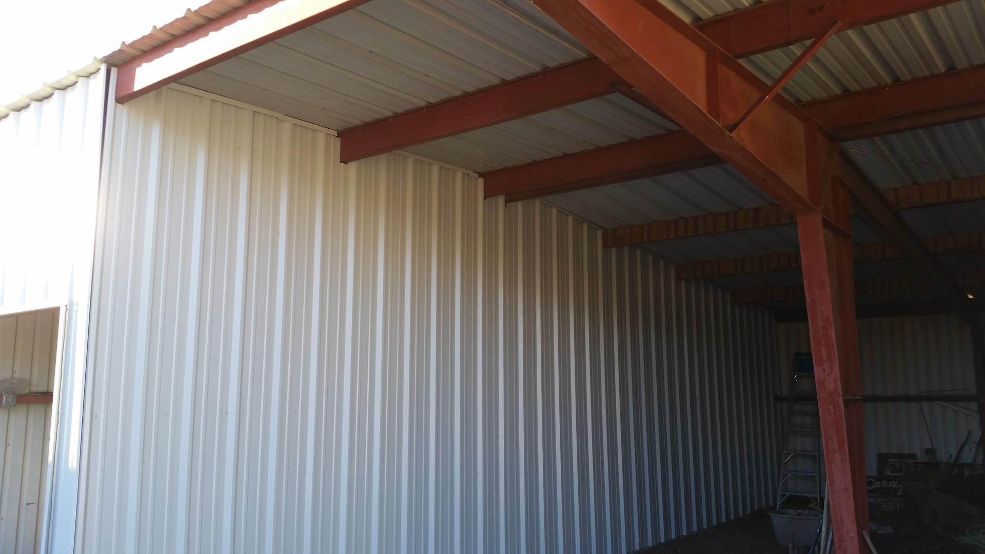 Metal-sided industrial building with a white roof overhang and red support beams