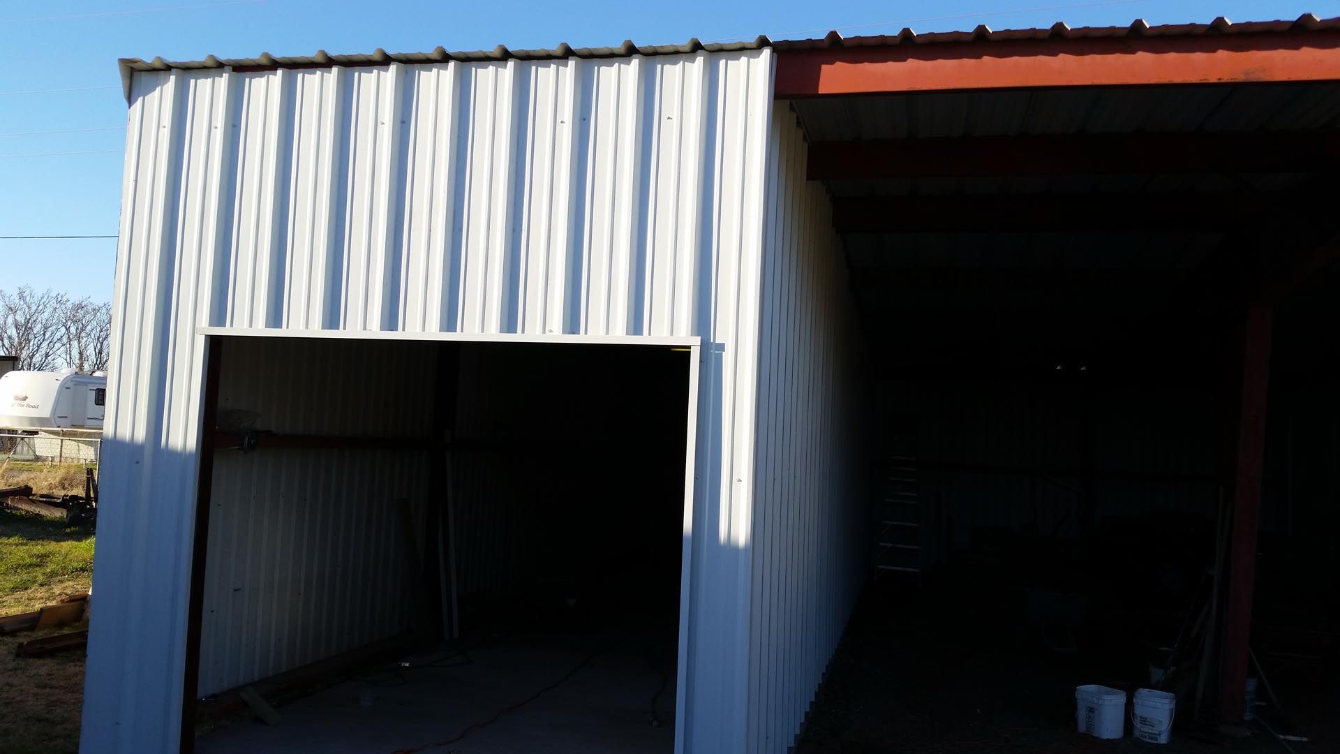 Two open metal storage sheds, one white and one dark inside, under bright daylight.