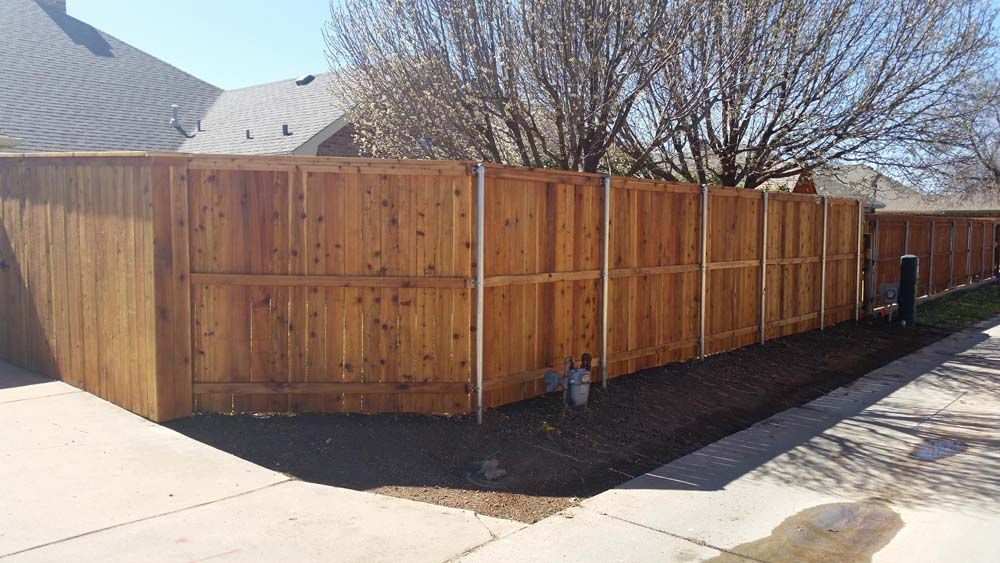 Wooden privacy fence along a driveway beside a house, with a leafless tree overhead.