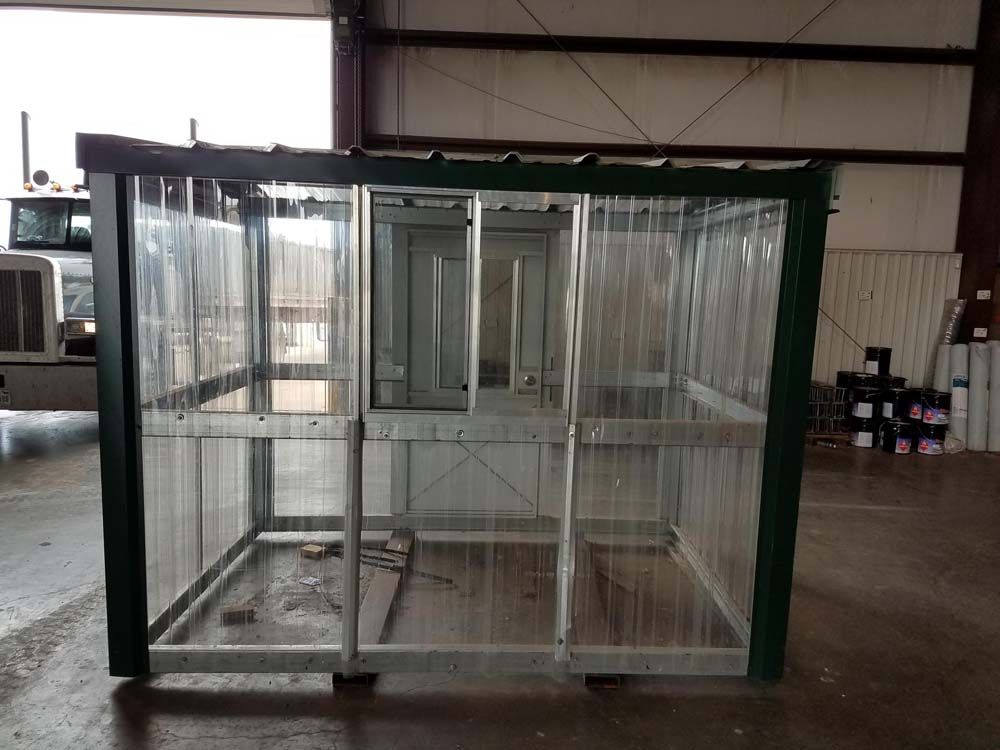 Empty green metal cage in a warehouse, with clear panels and a small door.