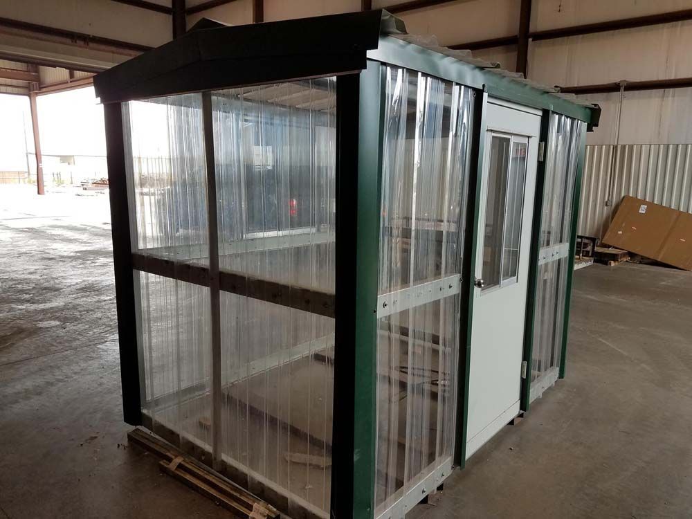 Small green-framed glass enclosure or booth in an industrial warehouse area