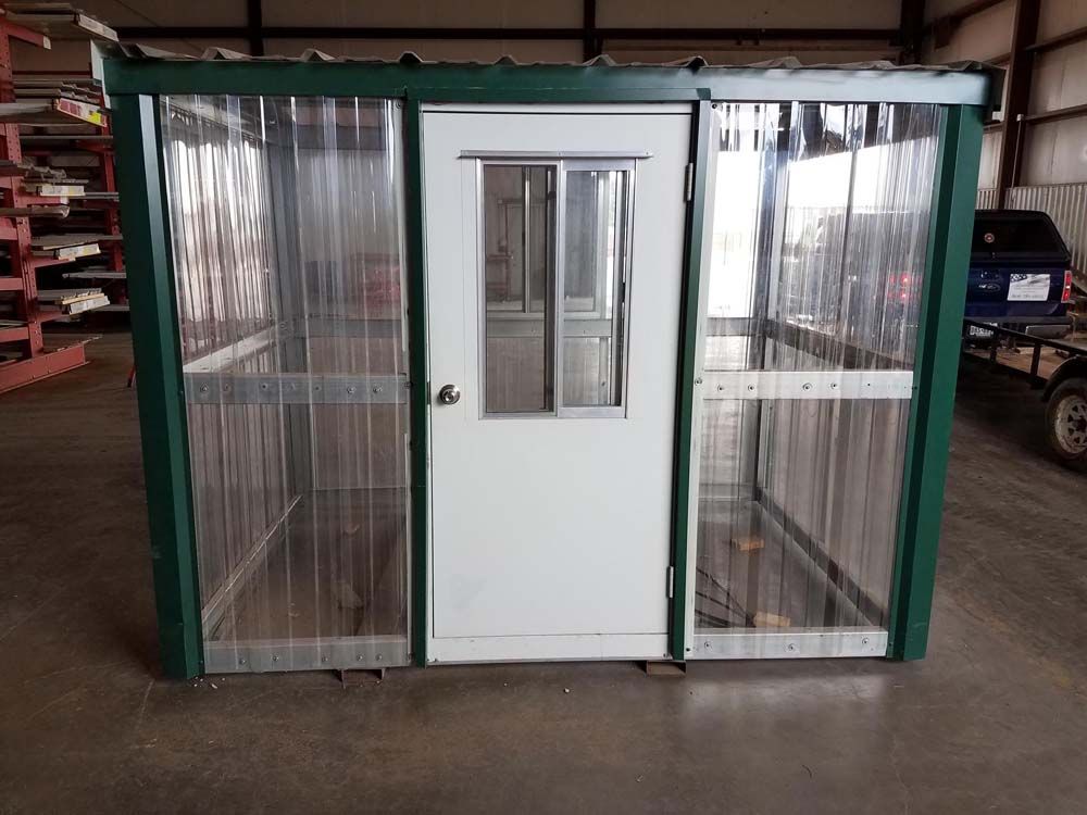 Small green-framed glass enclosure with a white door and narrow window on a concrete floor.