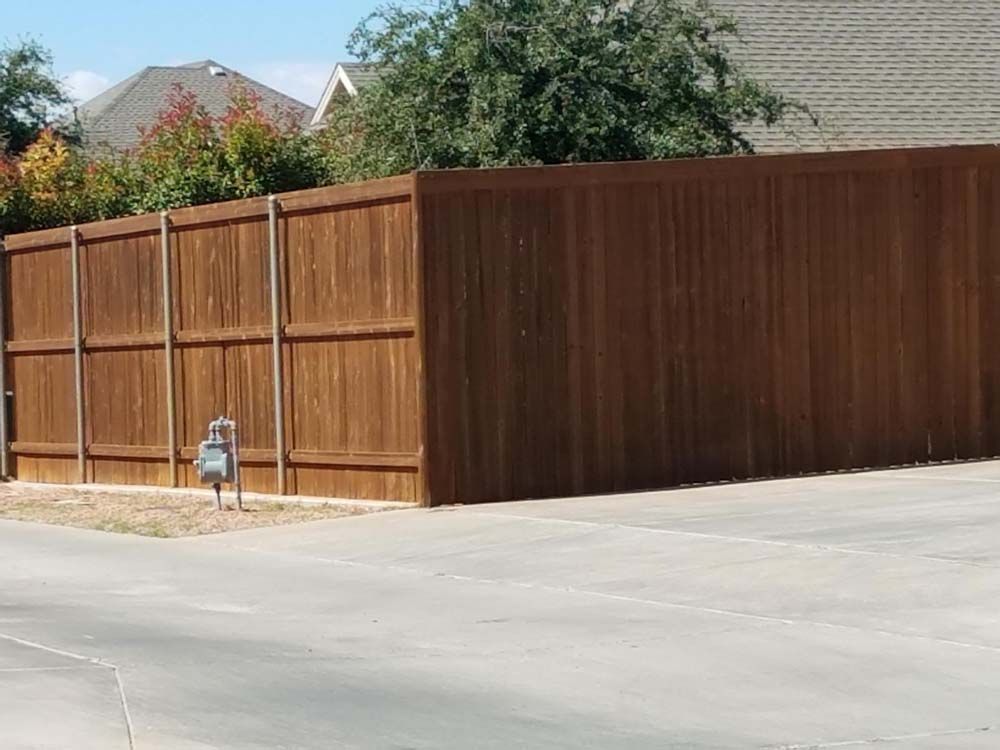 Wooden privacy fence beside a paved driveway, with a fire hydrant and trees in the background.