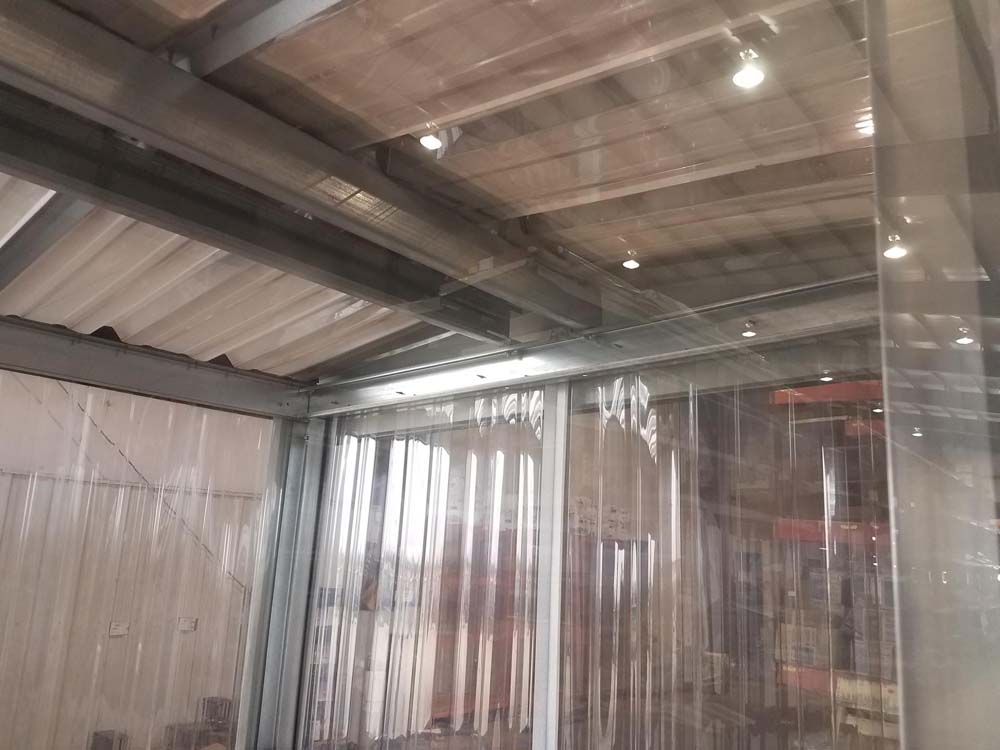 Plastic sheeting hanging in an industrial warehouse with metal beams and overhead lights