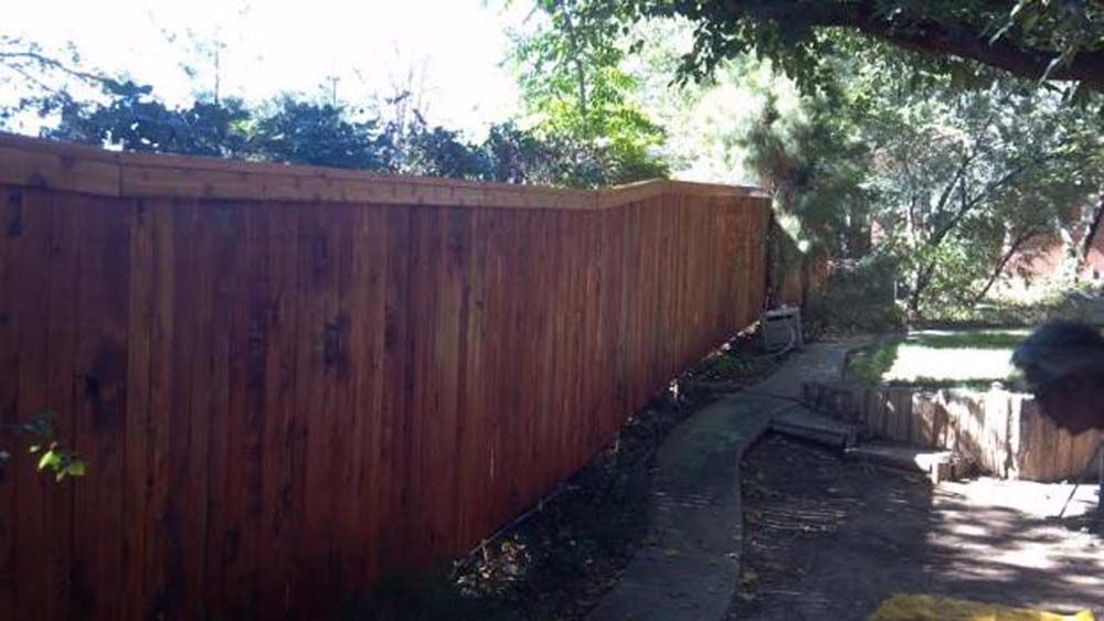 Wooden fence lining a dirt path beside a small creek in a shaded outdoor area