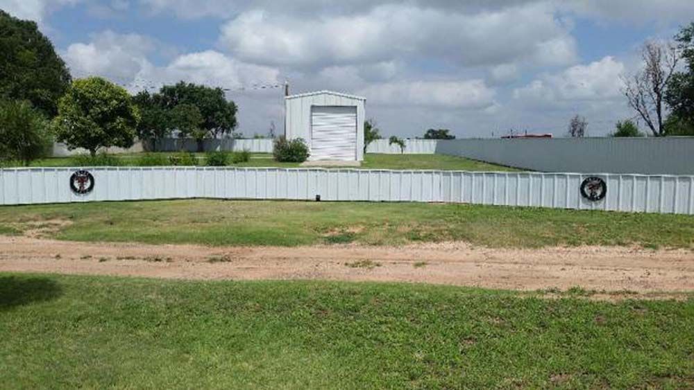 White barrier wall with round emblems beside a grassy field and water under a cloudy sky