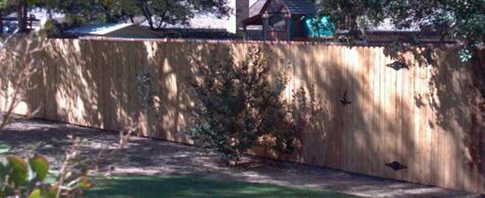 Wooden fence in a shaded yard with grass and trees behind it