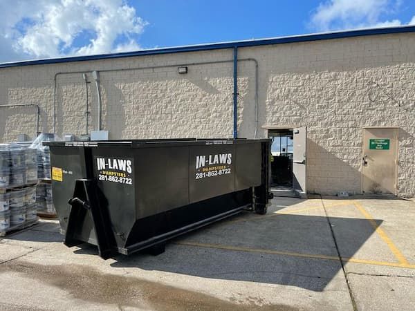 A large black dumpster is parked in front of a building.