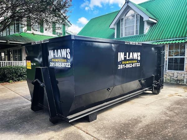 A dumpster is parked in front of a house with a green roof.