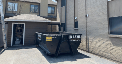 A dumpster is parked in front of a brick building.