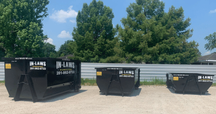 Three dumpsters are parked next to each other in a gravel lot.