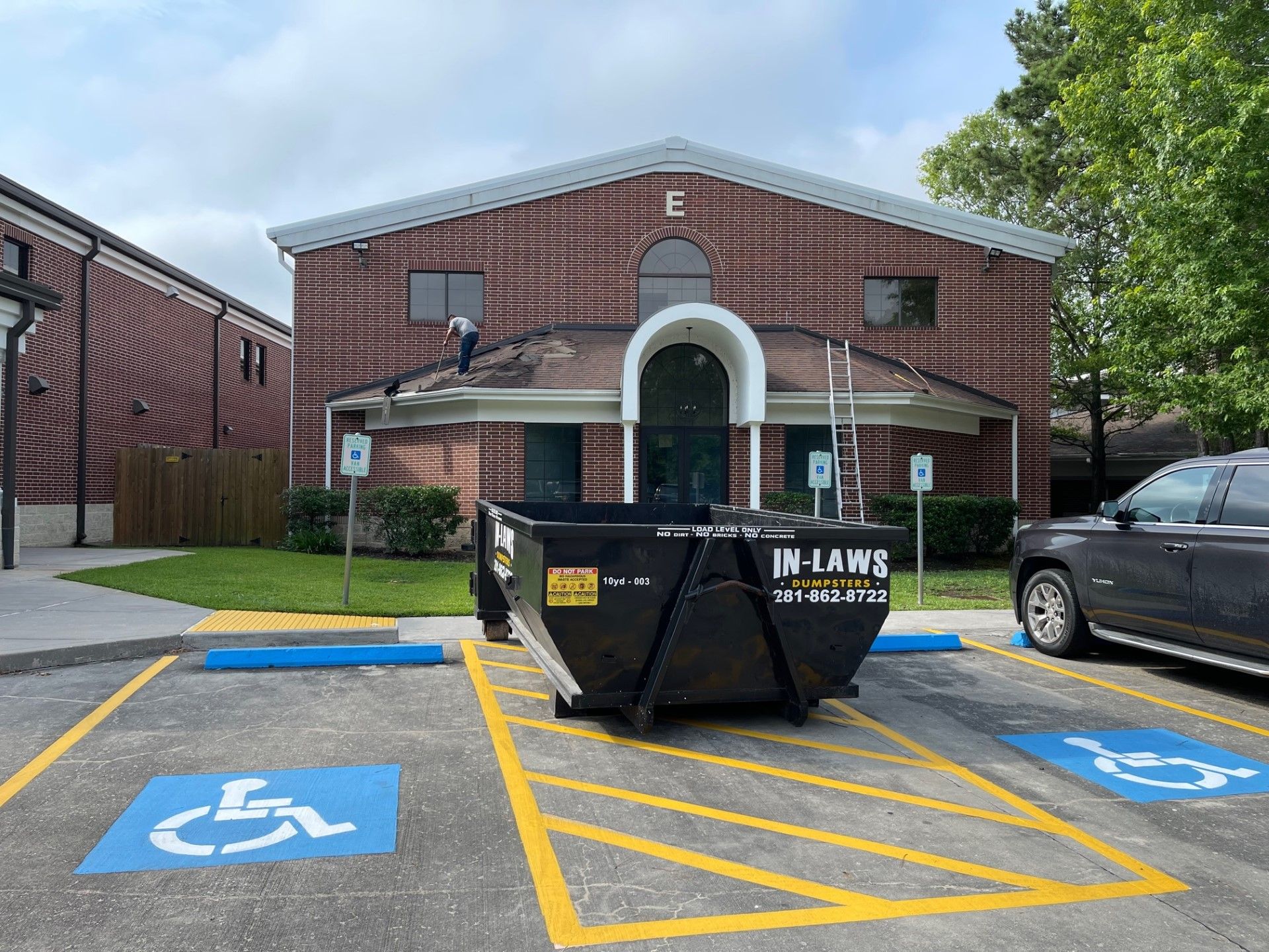 A dumpster is parked in a handicapped parking spot in front of a brick building.