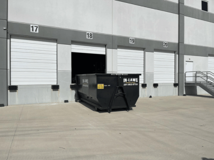 A large black dumpster is parked in front of a building.