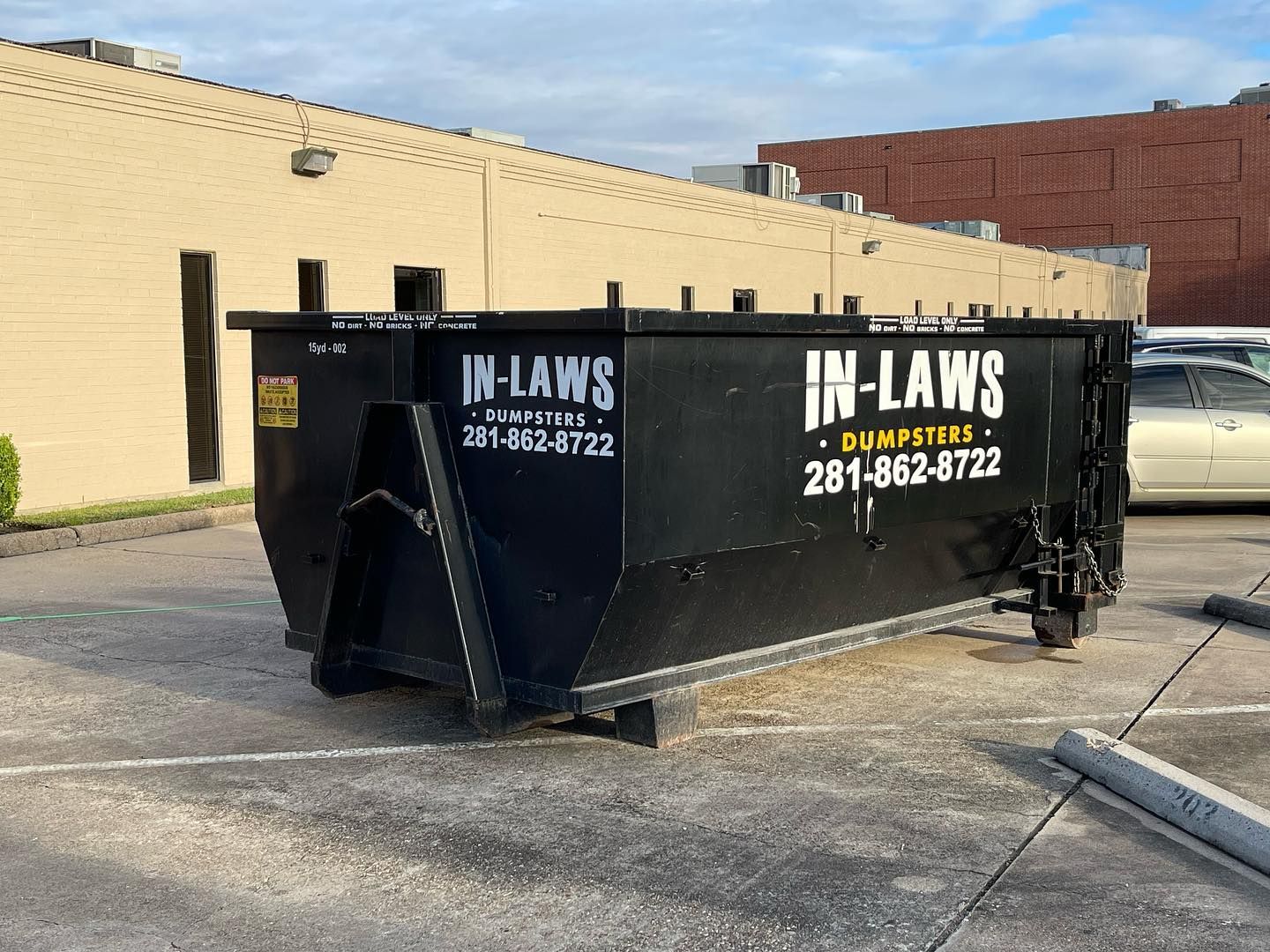 A large black dumpster is parked in a parking lot in front of a building.