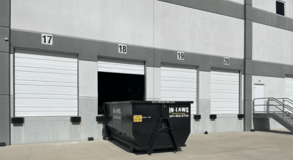 A dumpster is parked in front of a building with a number 17 on it.