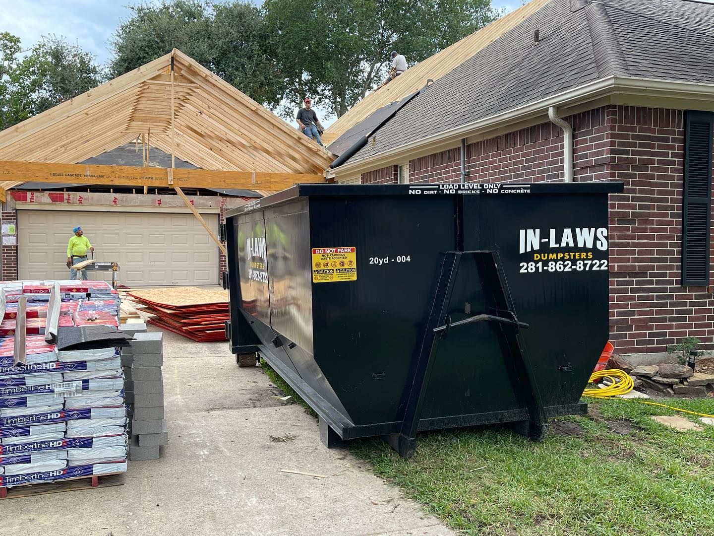 A dumpster is parked in front of a house under construction.