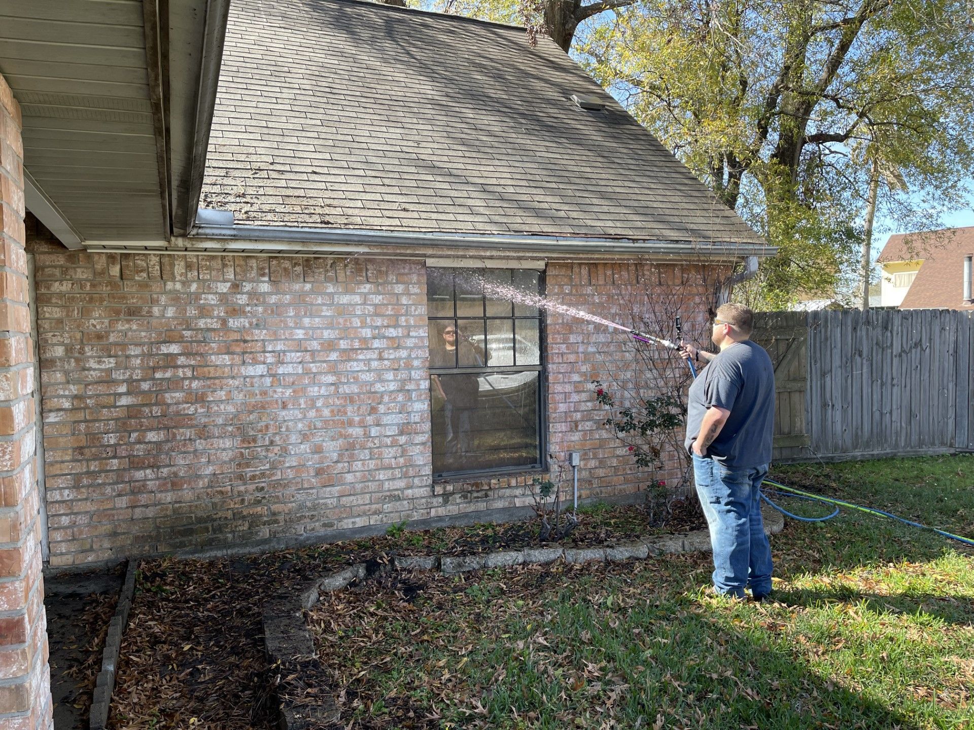 A man is spraying water on the side of a brick house.