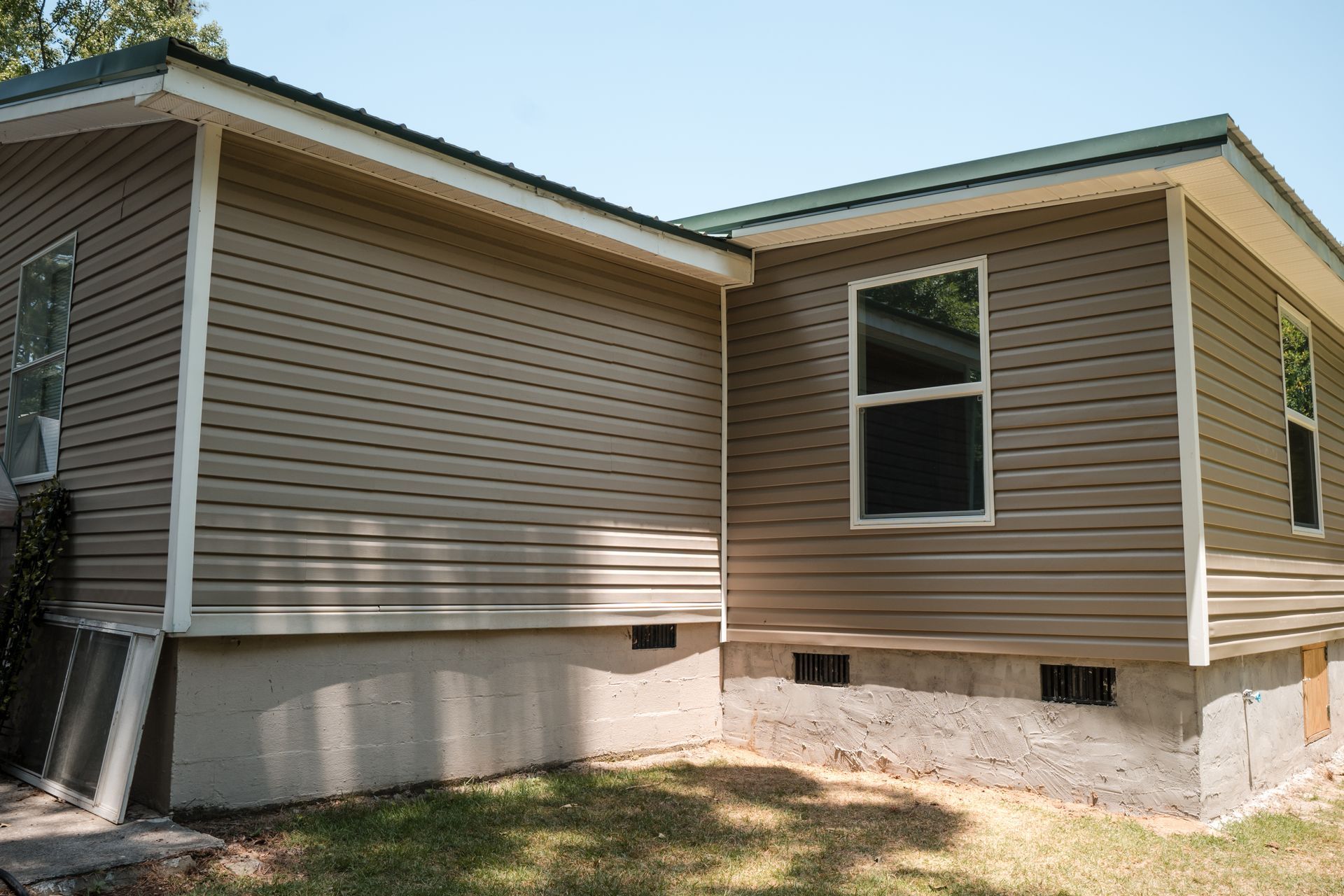 Tan house exterior with beige siding, white trim, and a small window over a concrete foundation.