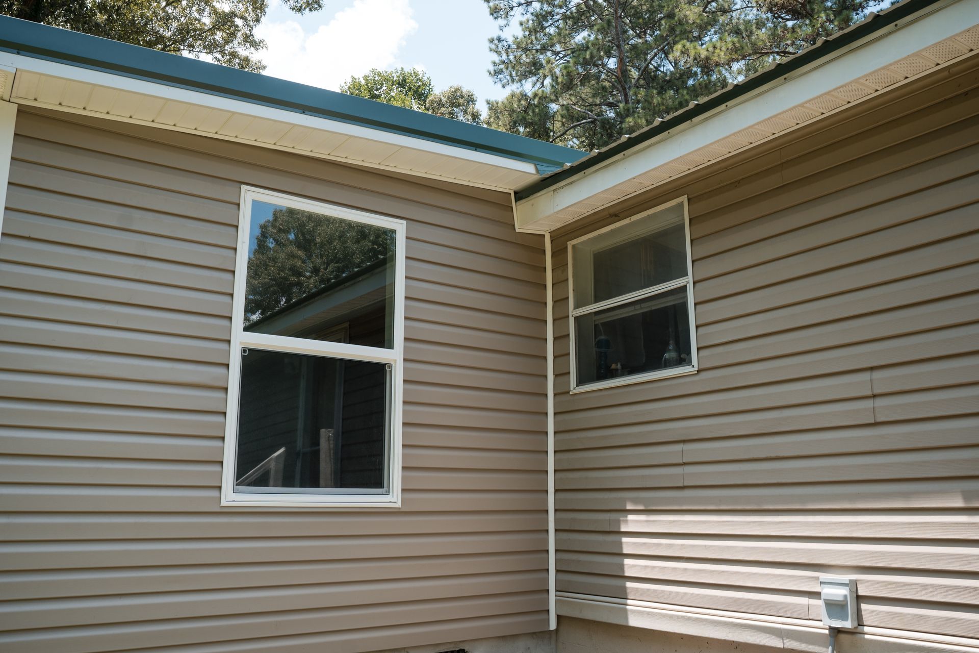 Beige house exterior with two windows and a white downspout beneath a blue roof trim