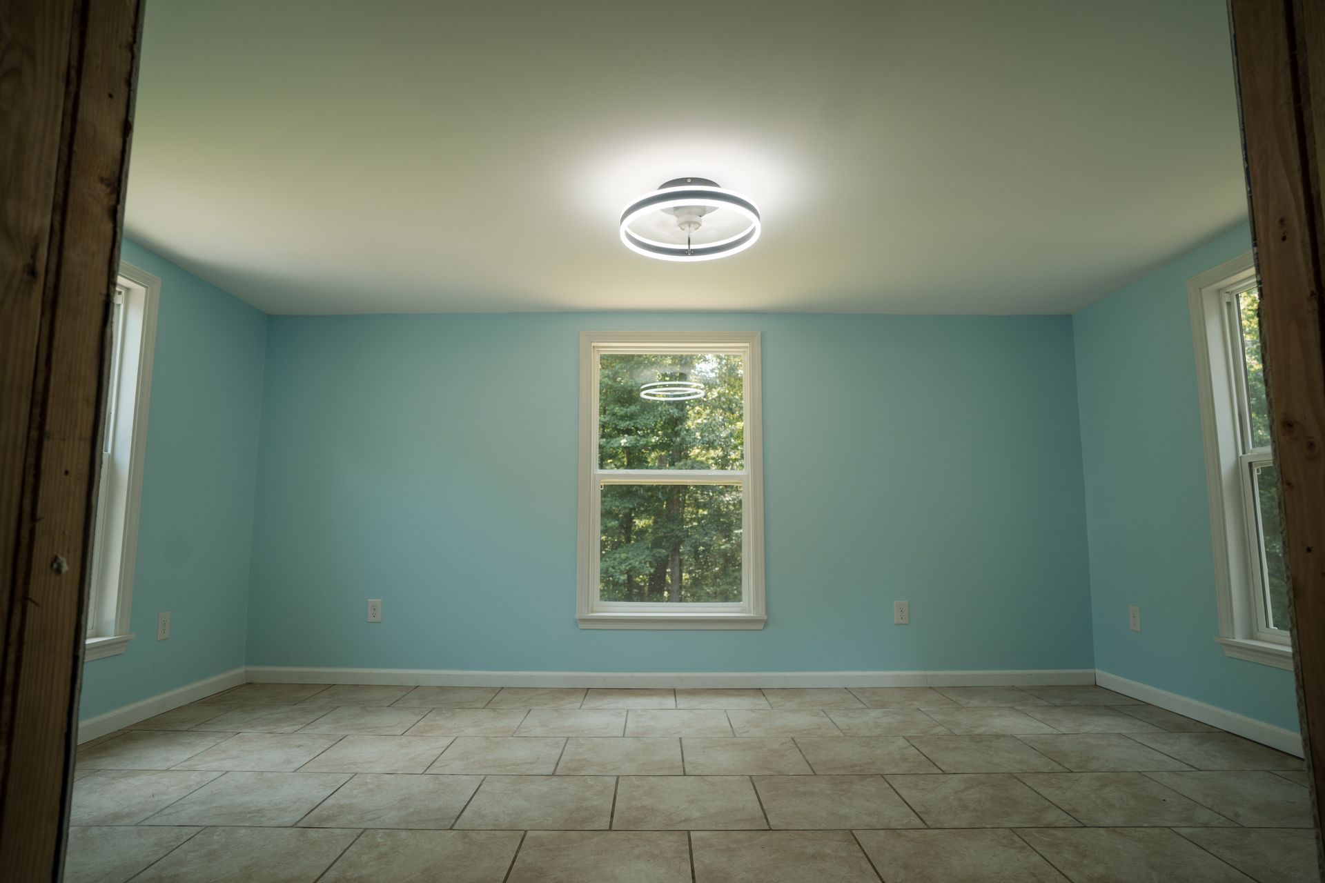 Empty room with light blue walls, tiled floor, and three windows under a ceiling light.