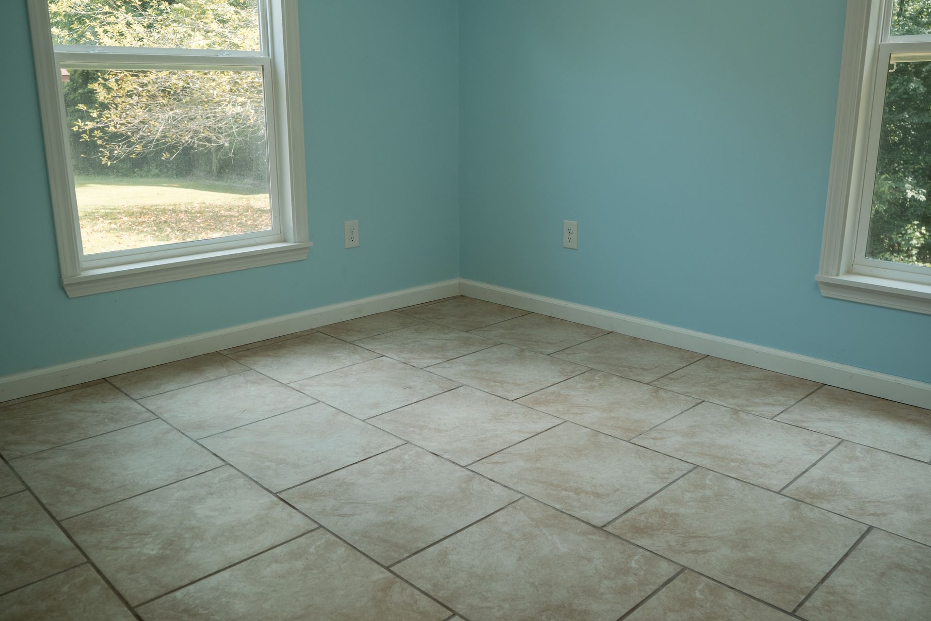 Empty light-blue room with tiled floor and two windows letting in daylight