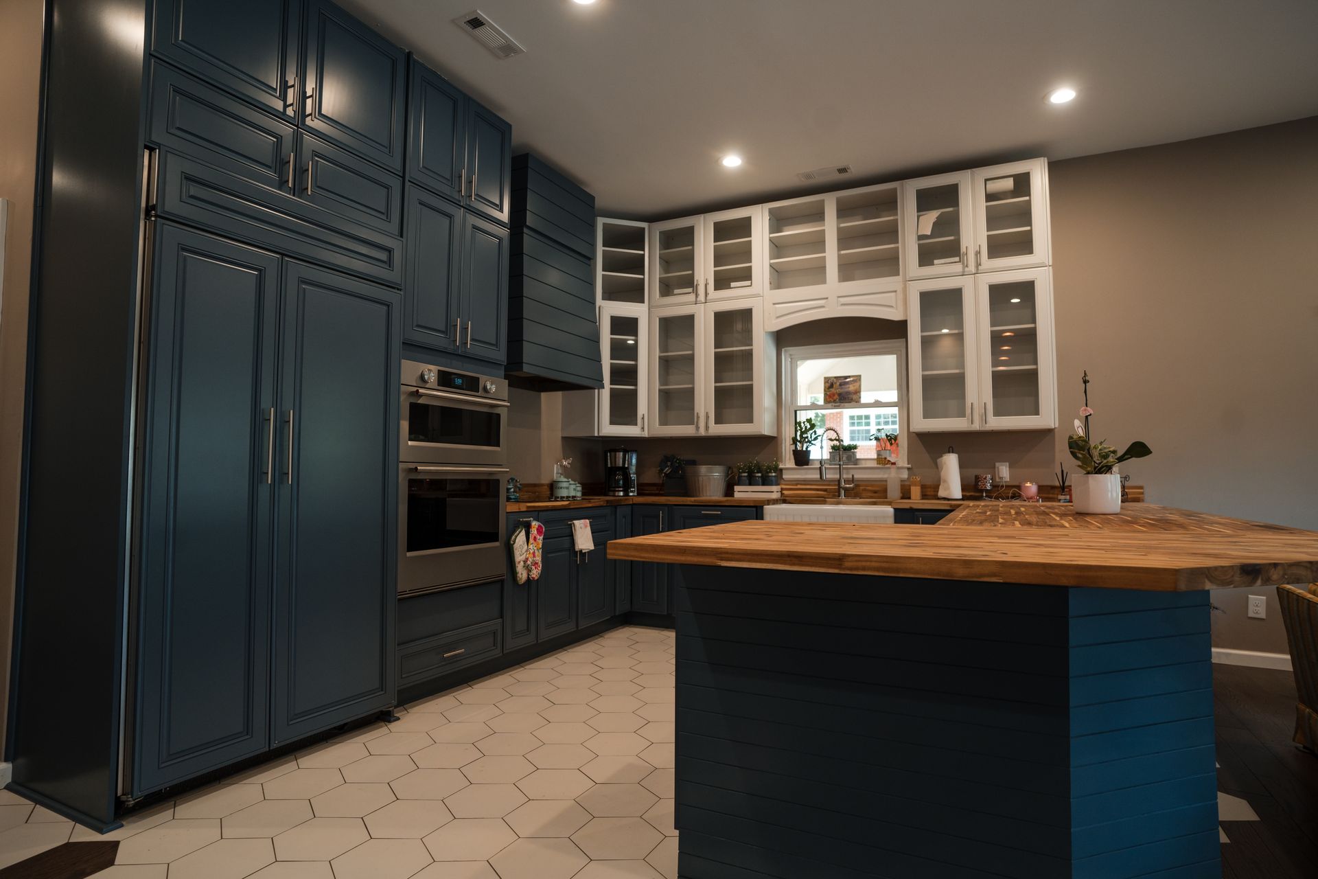 Modern kitchen with dark blue cabinets, white glass-front cupboards, and a large wooden island.