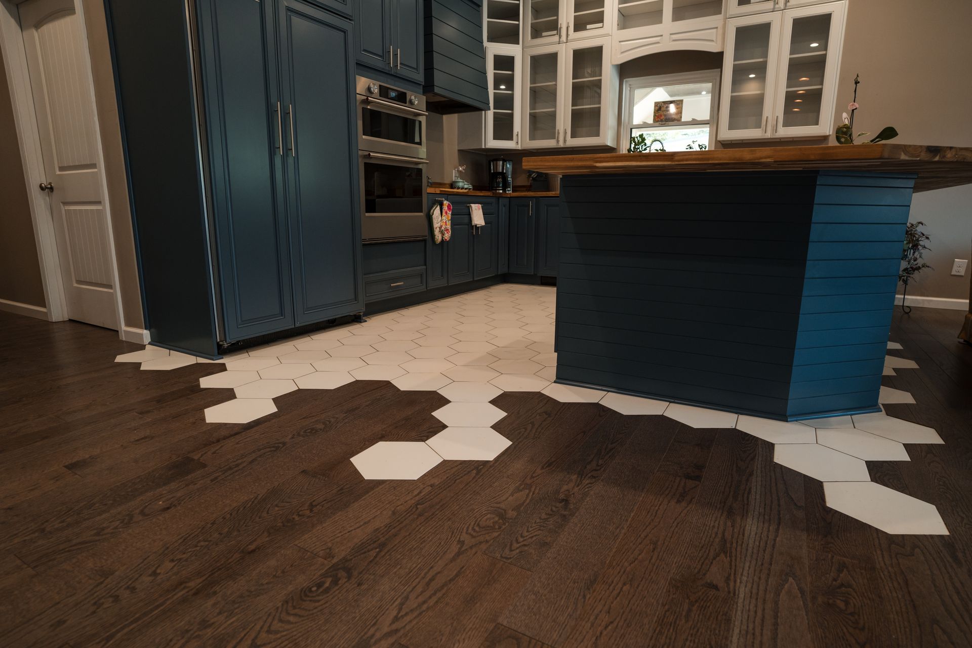 Kitchen with dark wood floor, blue cabinets, and white hex tile pattern around the island.