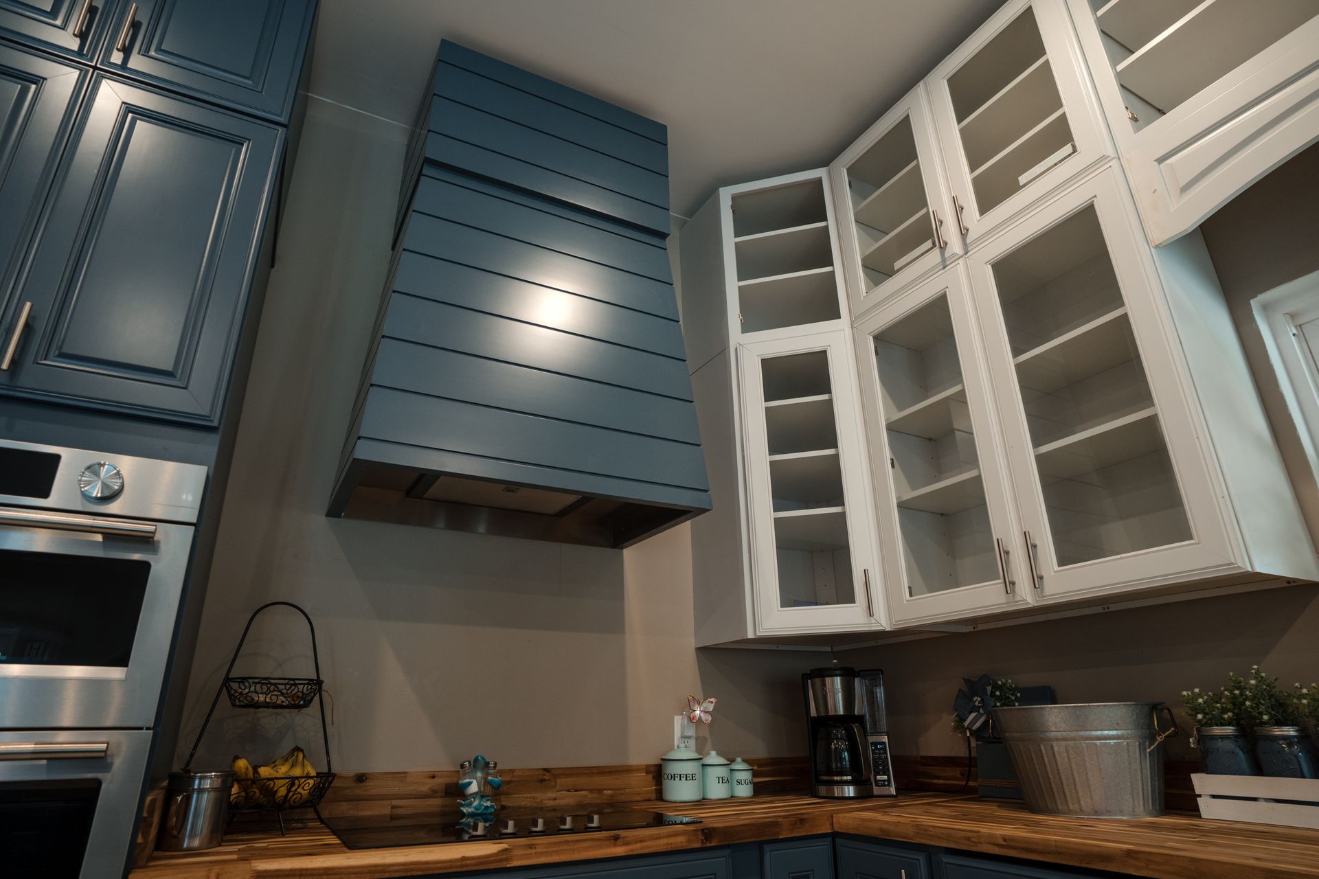Blue and white kitchen cabinets above a wooden countertop with appliances and a tiled backsplash