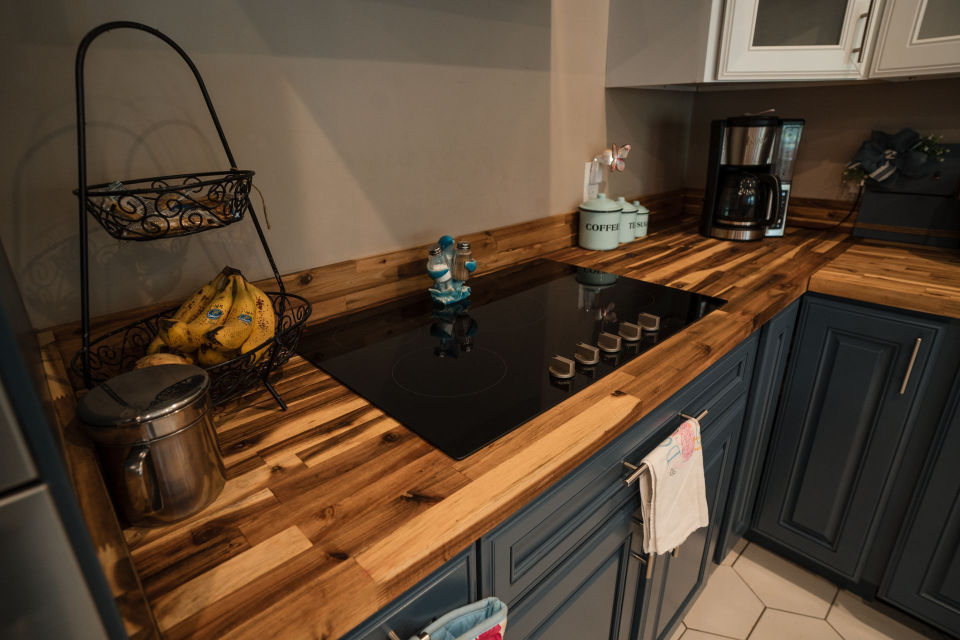Compact kitchen counter with black cooktop, wooden countertops, blue cabinets, and a fruit basket