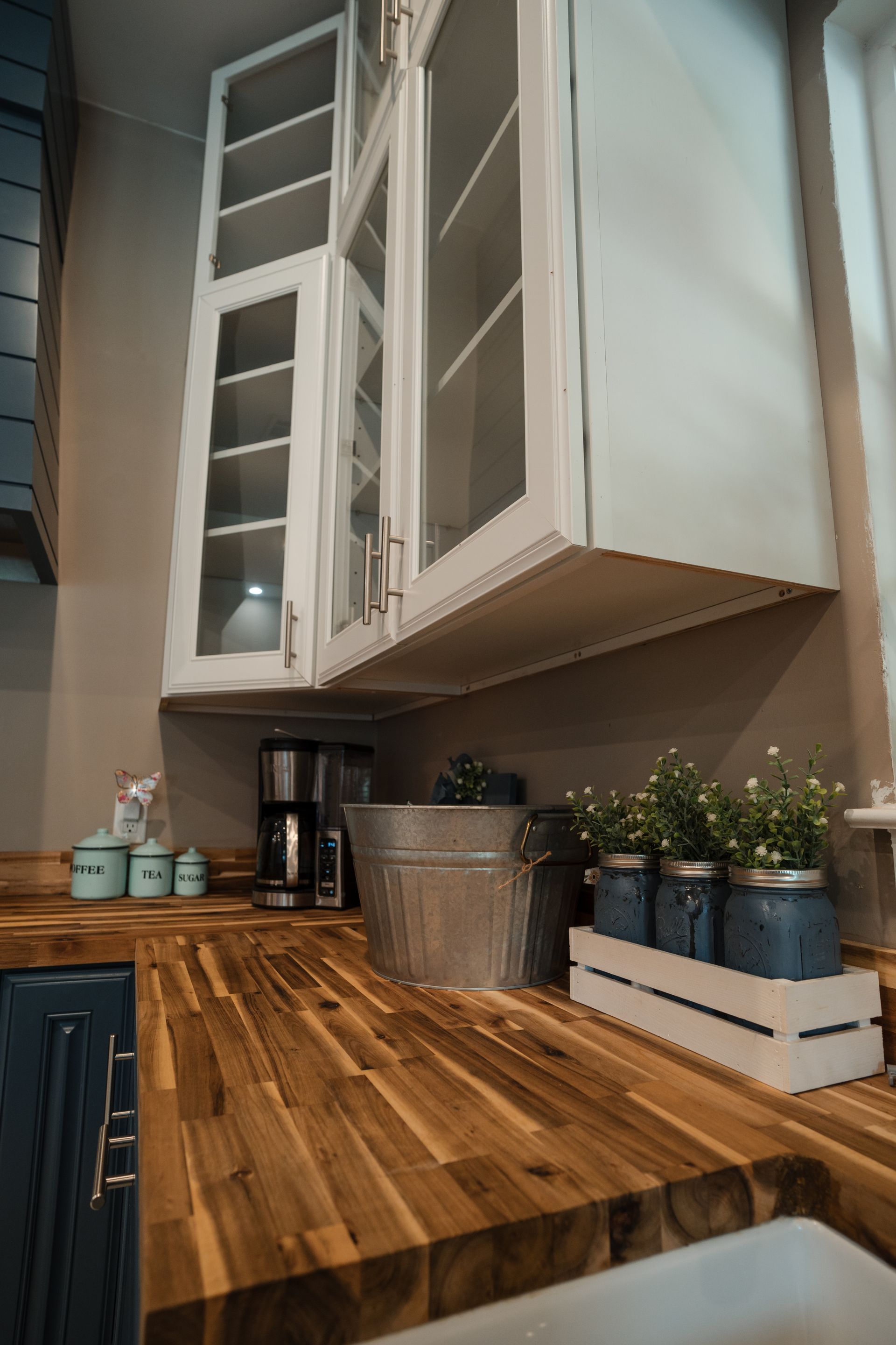 Modern kitchen counter with butcher-block top, white cabinets, coffee maker, and potted herbs on a tray.
