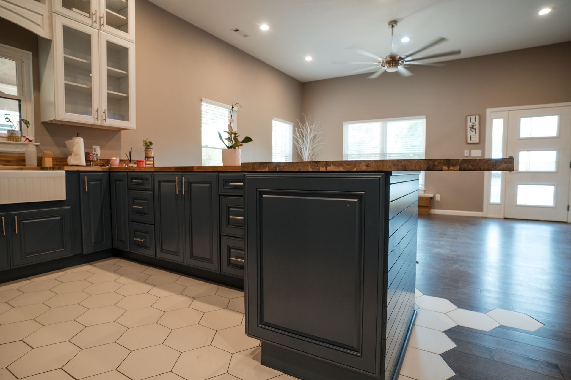 Modern kitchen with dark island cabinets, white tile floor, and open dining area with large windows