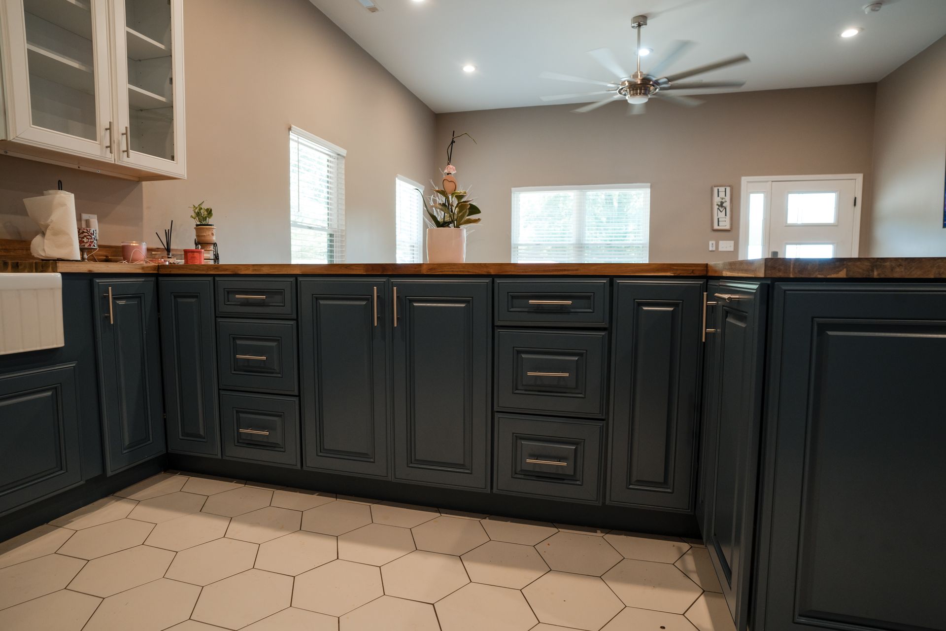 Kitchen with dark blue cabinets, white hex tile floor, and windows above a light-colored island.