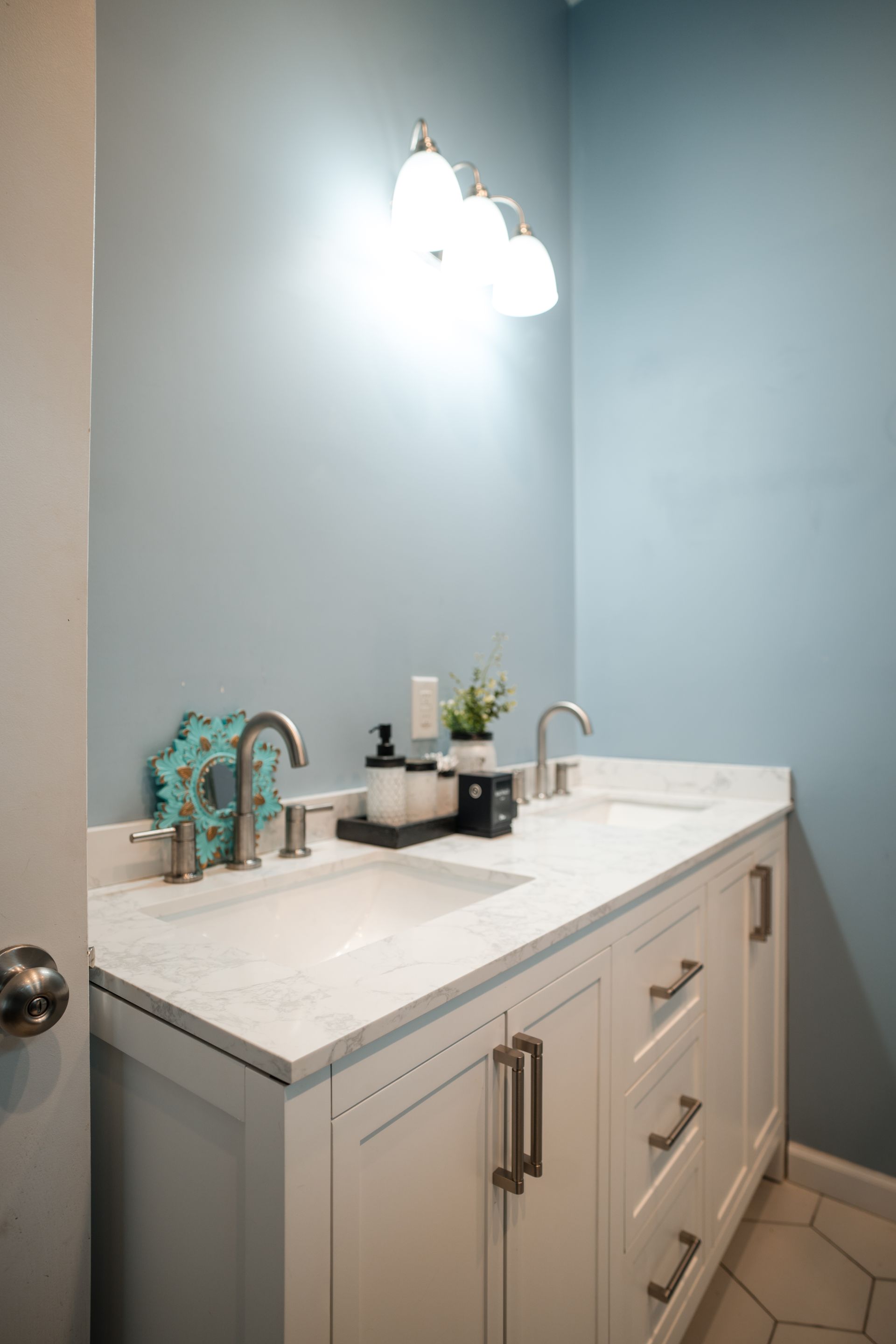 Bathroom vanity with white countertop, brushed nickel faucet, and light blue walls under a double sconce.